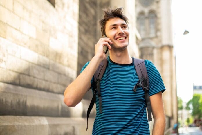 Portrait handsome smiling guy walking with bag and talking with cellphone in city - stock image