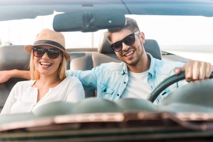 Happy beautiful young woman in hat driving car during road trip