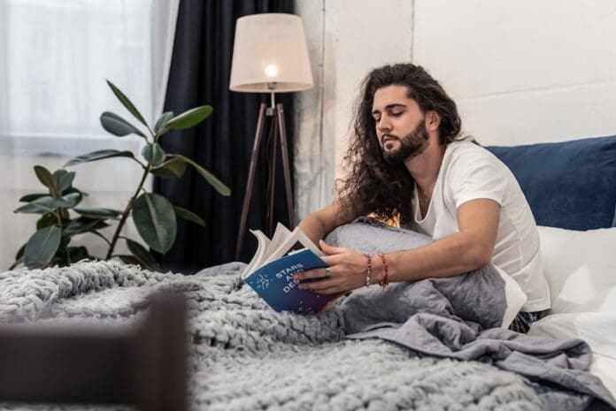 young man reading about astrology in bed