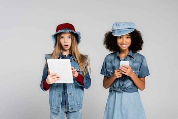 Excited interracial kids in trendy clothes using smartphone