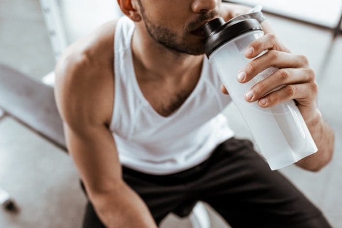 Cropped view of sportsman drinking protein milkshake at gym