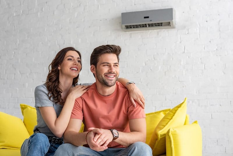 Happy couple sitting on yellow sofa under air conditioner