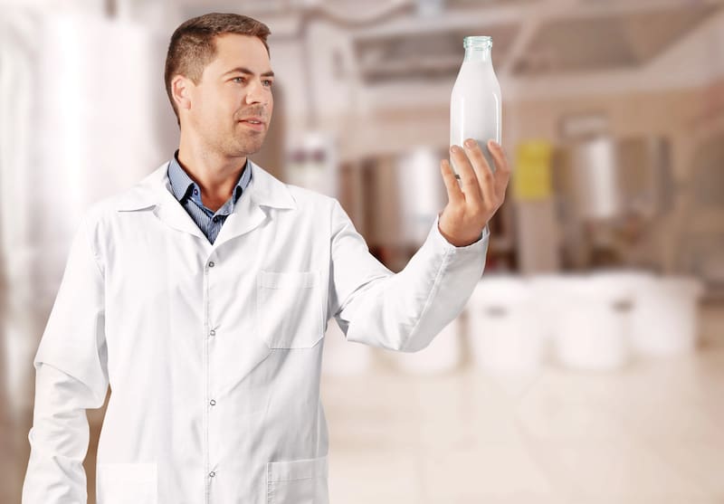 Professional expert with glass bottle of milk on blurred dairy