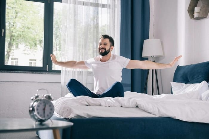 young man brown hair waking up at home morning blue curtains