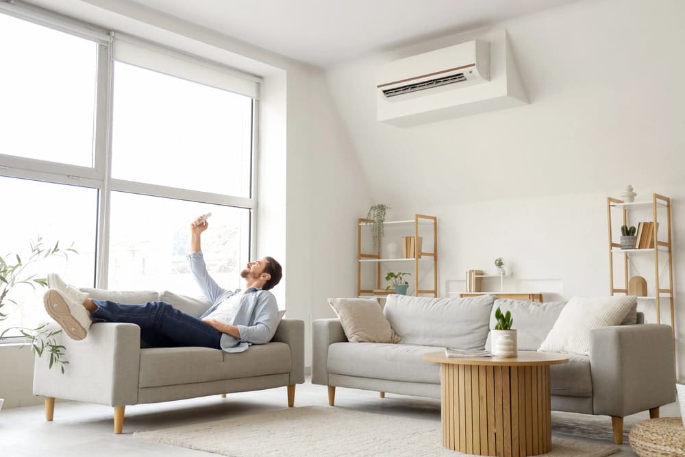 Lying young man turning on air conditioner in living room